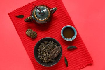 Bowl with dry leaves, teapot, cup of tasty tea and dry pressed tea on red background
