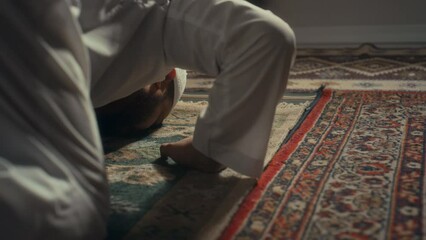 Rear ground level footage of observant muslim man praying to Allah and taking sujud position expressing his gratitude at home