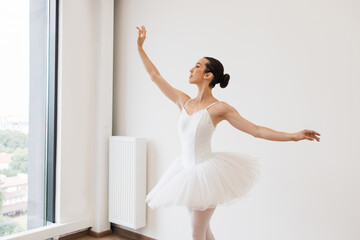 Fototapeta premium Young Caucasian ballet dancer practice wearing white swan skirt in studio, active lifestyle. Ballet student practicing classical dance pas in studio before performance.