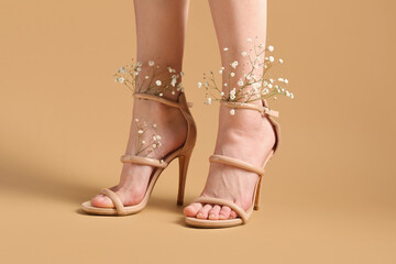 Legs of beautiful young woman in beige ankle straps shoes with white gypsophila flowers on beige...