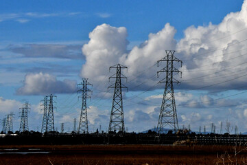 Electrical transmission towers silhouetted by white cumulus clouds adjacent to San Francisco Bay