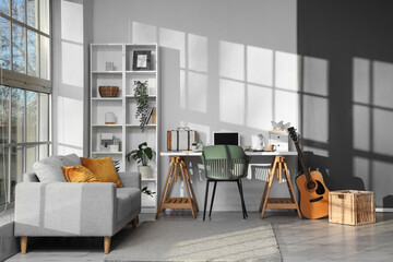 Interior of stylish office with workplace, shelving unit, sofa, guitar and laptop