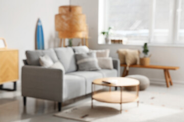 Stylish interior of light living room with comfortable sofa, table, carpet and lamp, blurred view