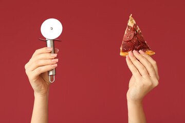 Female hands holding pizza slice and pizza cutter on red background