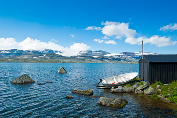 Boat on the shore of Lake Finsevatnet, snowy mountains and glacier Hardangerjokulen in Finse,...