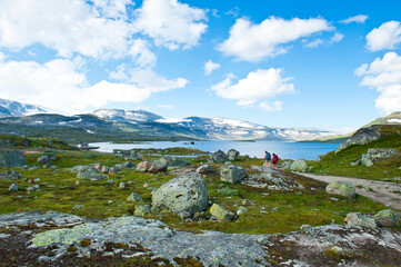 Tourists hiking towards dam of Lake Finsevatnet, snowy mountains and glacier Hardangerjokulen in Finse, Norway - 750961007