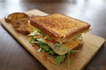 delicious toasted club saandwich with vegetables dressing and baked potatoes on a wooden board