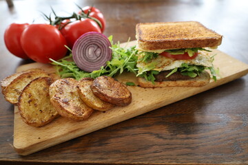 delicious toasted club saandwich with vegetables dressing and baked potatoes on a wooden board
