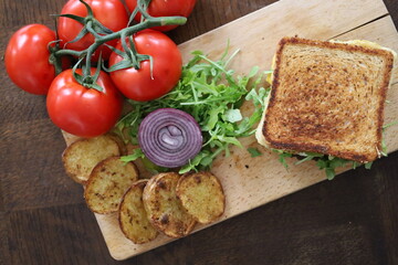 topview flatlay of delicious toasted club saandwich with vegetables dressing and baked potatoes on a wooden board