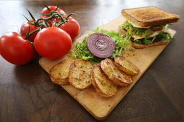 closeup delicious toasted club saandwich with vegetables dressing and baked potatoes on a wooden board