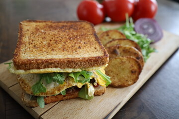 closeup delicious toasted club saandwich with vegetables dressing and baked potatoes on a wooden board