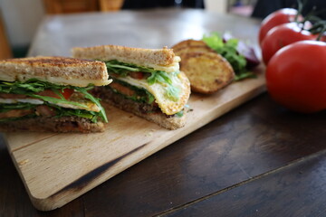 delicious toasted club saandwich with vegetables dressing and baked potatoes on a wooden board