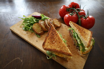 delicious toasted club saandwich with vegetables dressing and baked potatoes on a wooden board