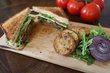 upper view of delicious toasted club saandwich with vegetables dressing and baked potatoes on a wooden board