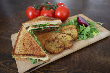 upper view of delicious toasted club saandwich with vegetables dressing and baked potatoes on a wooden board