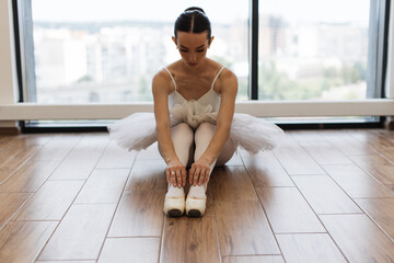 Classical Ballet dancer. Beautiful Caucasian graceful female ballerina in tutu skirt sitting at wooden floor and stretching while practice split ballet position, front view.