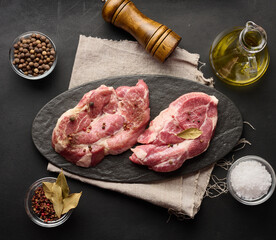 Two raw pork neck steaks on a board and spices for cooking. Top view