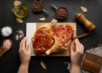 Raw chicken drumsticks seasoned on a wooden board, accompanied by salt and peppercorns, viewed from...