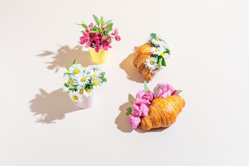 Creative composition of croissants adorned with fresh flowers on a soft pastel backdrop