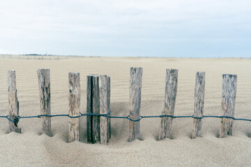 une barrière en bois ensevelie dans le sable avec une personne de dos en fond