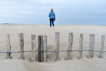 une barrière en bois ensevelie dans le sable avec une personne de dos en fond - 750965859