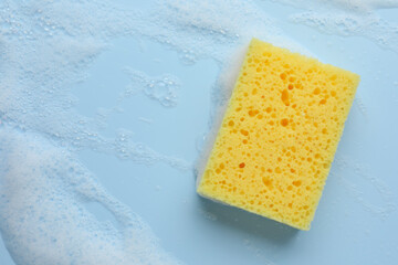 Yellow sponge with foam on light blue background, top view. Space for text