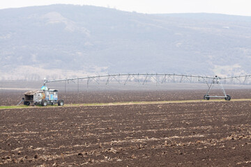 Fototapeta na wymiar A tractor plows a field with irrigation system under a vast sky