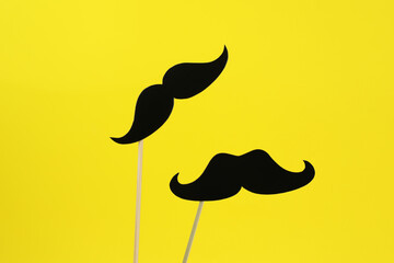 Fake paper mustaches on sticks against yellow background