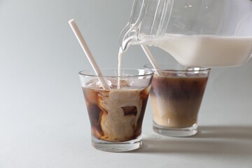 Pouring milk into glass with refreshing iced coffee on grey background, closeup. Space for text