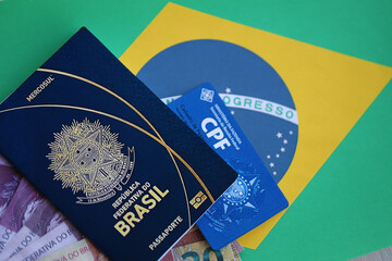 Passport book of Federative Republic of Brazil, CPF taxpayer card and brazilian reais money bills on flag background close up