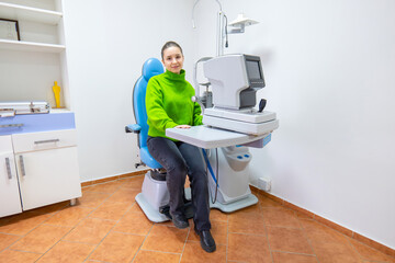 A woman in a green sweater is seated in the ophthalmologists chair