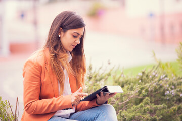 young businesswoman in professional attire, utilizing a tablet in an outdoor setting - 750972261