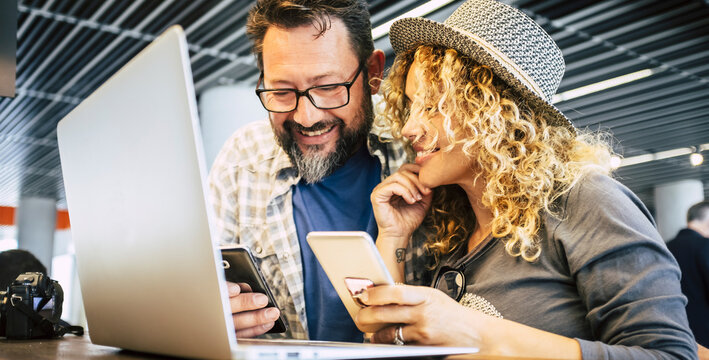 Young millennial couple working together in coworking space with mobile phones and laptop computer. Modern online job lifestyle people. Happy man and woman travel. Social media business activity web