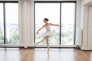 Young graceful ballet dancer rehearsing performance in white spacious hall. Caucasian ballerina...