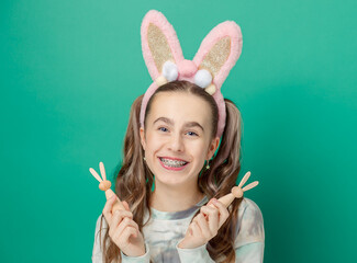 Girl with joyful smile, wearing glittery pink bunny ears holding wooden bunny figures, showcases her braces