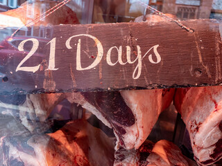 21 days dry aged hung beef on display in the widow of a butcher retail store. - Powered by Adobe