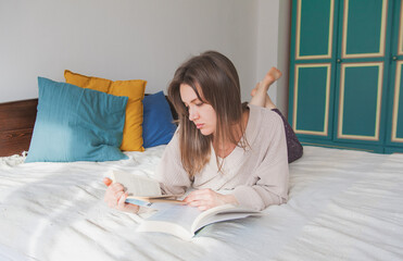 Young woman lying down on the bed and studying with reading books at home
