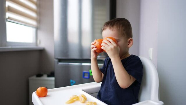 Lovely Caucasian baby boy eats the fruit and taps the tangerines. Little kid enjoying healthy food.