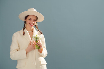 Fashionable happy smiling woman wearing white hat, boucle coat, pearl necklace, holding spring...