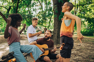 A small group of multiracial friends dancing and playing guitar in park.