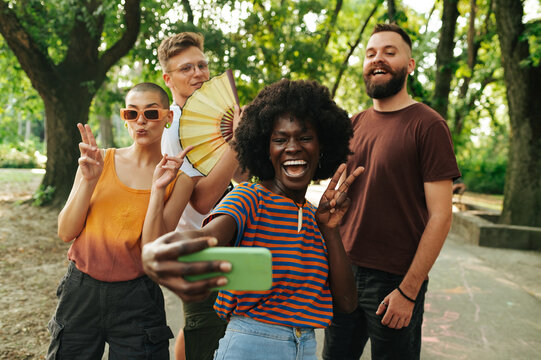 Four young people walking in park and taking a selfie together.