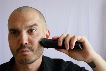 bald man using an electric shaver to trimm his hair and beard