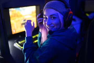 Smiling woman gamer looking at the camera while playing video game in a gameroom