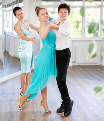 Experienced female dancer teaches tango to pair of teenagers in the ballroom