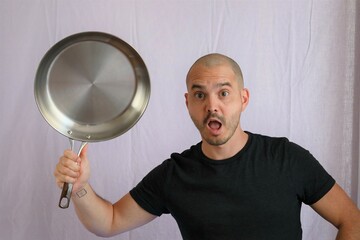 funny and expressive bald man in blue t-shirt  holding kitchen ustensils