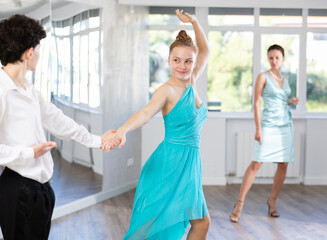 Enthusiastic teenagers, boy and girl in formal wear performing elegant waltz in pair in sunny hall...