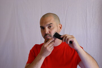 casual bald man in red t-shirt shaving his hair and beard 