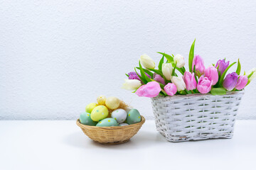 Easter eggs next to a wicker basket filled with natural fresh tulips. Greeting cards. White background.