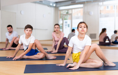 Fit woman, man and teenage girl and boy performing yoga exercises on gymnastic mats at yoga studio, physical, emotional and spiritual family health concept