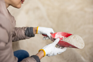 Closeup of red scoop with corn germ meal in hands of female farmer checking quality of livestock feed at dairy farm..